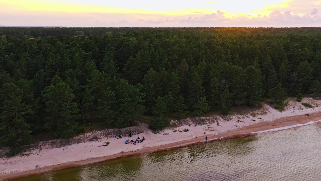 Golden hour drone shot of Melnsils Latvia, people sitting on sandy beach, sunset