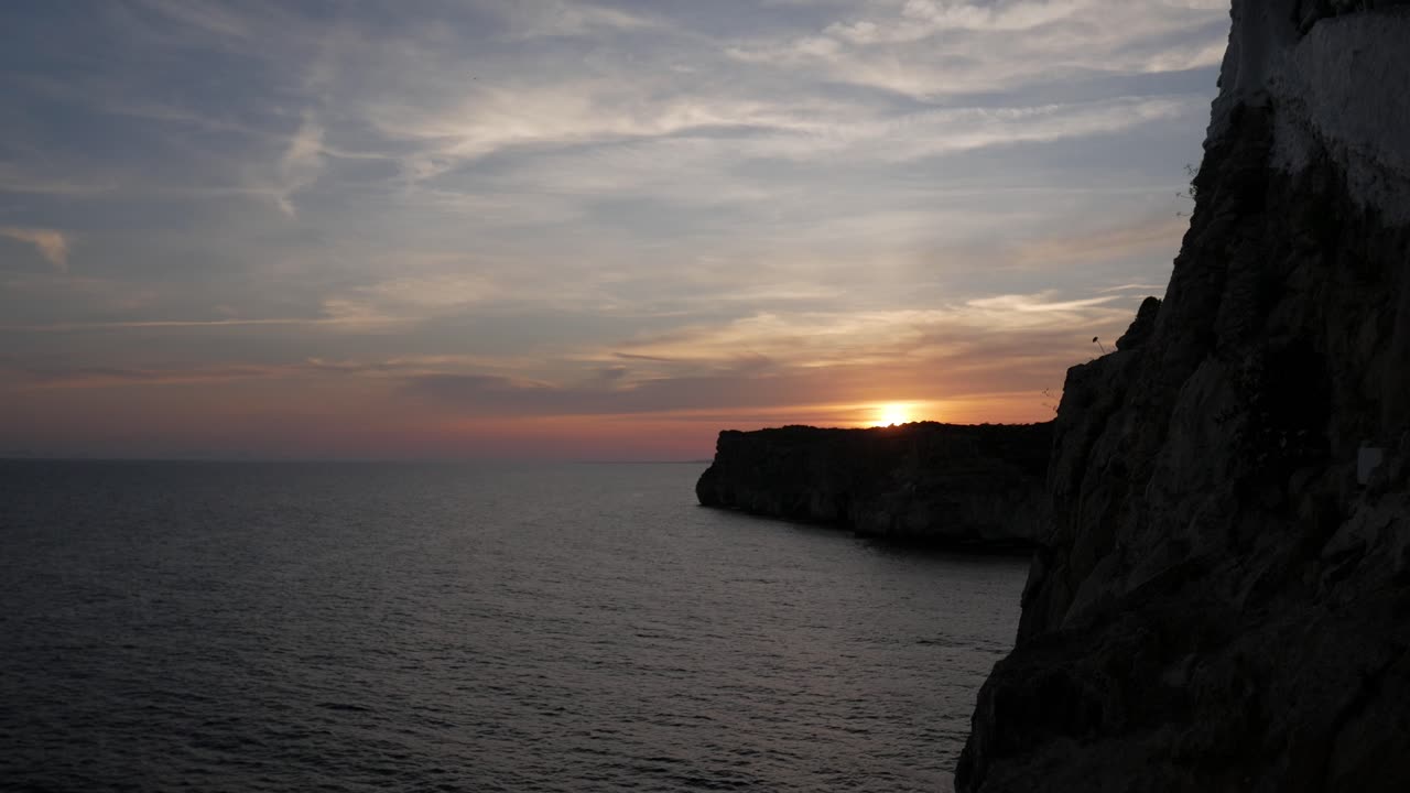A stunning sunset over the Cova D'En Xoroi coastline with a clear view of the sea