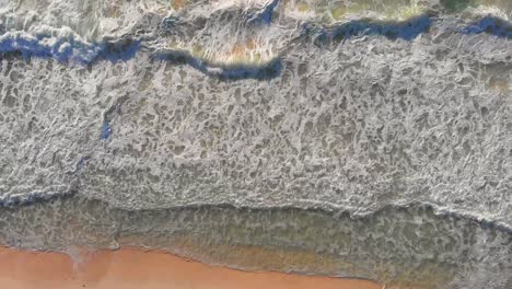 olas marinas tropicales que se estrellan en la arena dorada de la playa durante el amanecer - drones que se acercan, vista de arriba hacia abajo