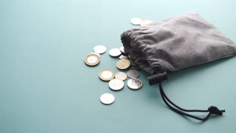 monedas derramadas de una pequeña bolsa sobre un fondo verde claro