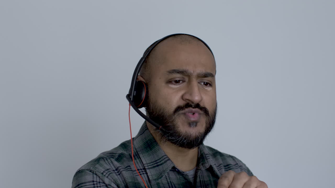 hombre asiático calvo del reino unido con auriculares hablando trabajando desde casa, gesticulando