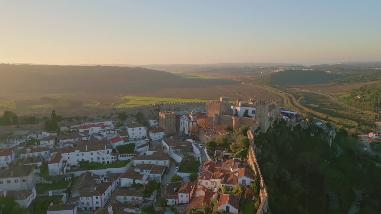 Aerial cozy village placed at green valley under evening sky. Ancient castle