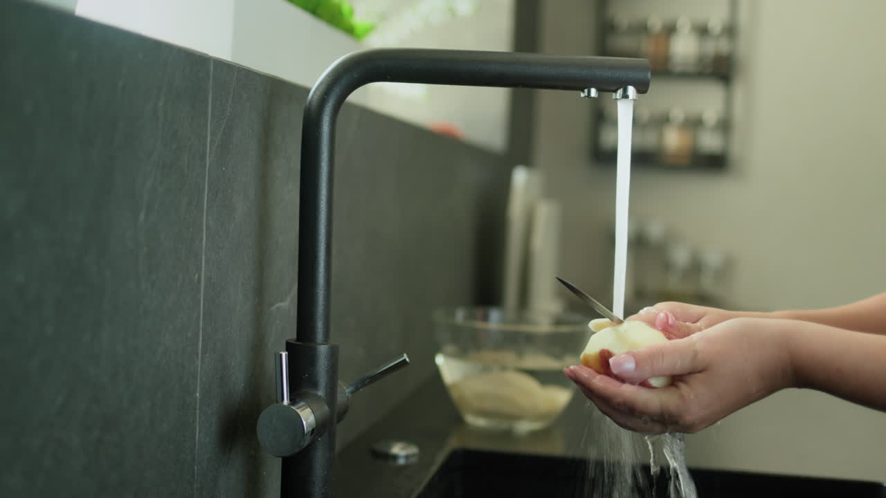 Person peels potatoes under running water from a kitchen faucet. 4k video