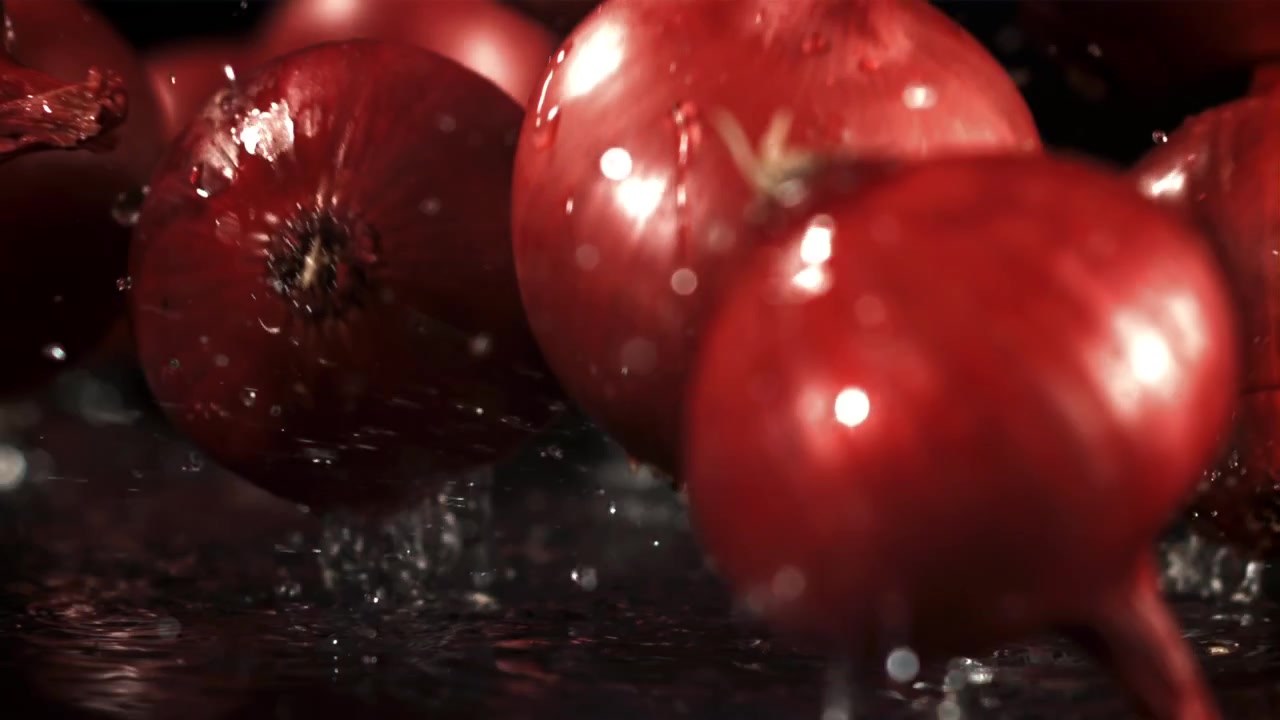 Rote Zwiebeln fallen in Zeitlupe mit Wasserspritzern