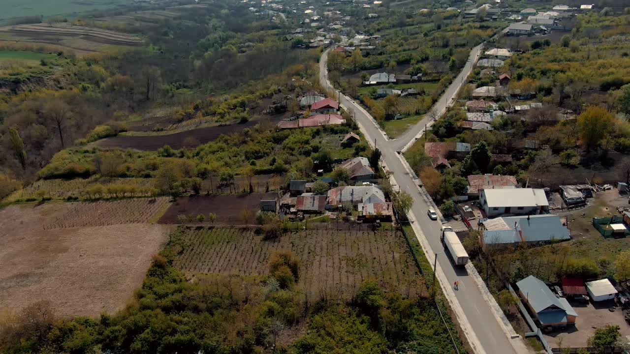 Aerial view over an old village road and houses, agricultural fields, surrounding hills, sunny day