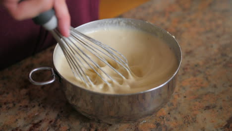 close up of a hand mixing ingredients in a steel bowl with a whisk