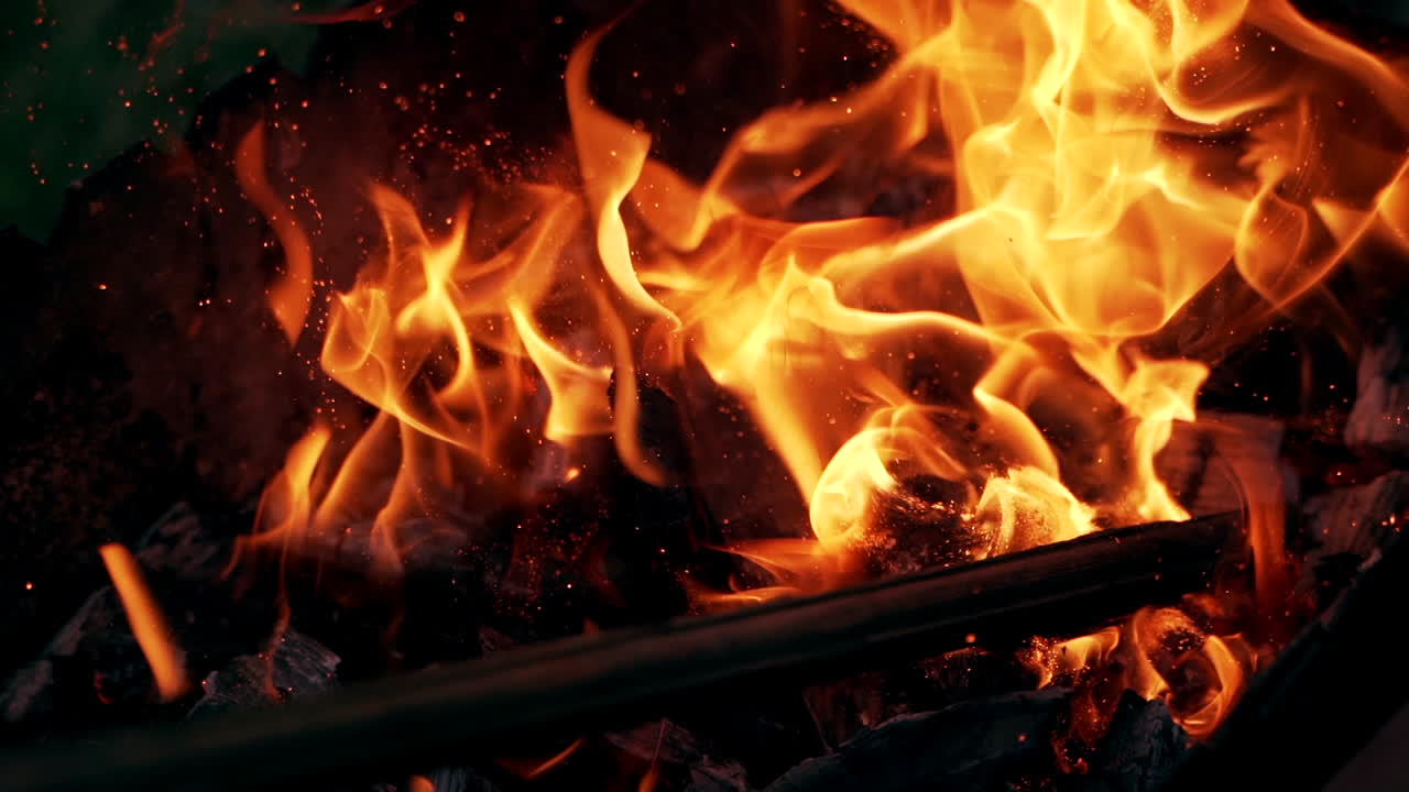 Bright sparkles flying from the fire at night. Wooden stick break smoldered logs in fire and flame becomes brightly outdoors. Slow motion.