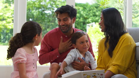 smiling family at home sitting on floor in lounge reading book together