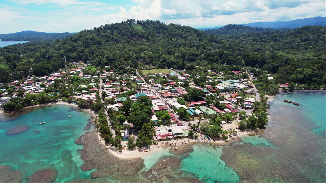 Wide aerial of downtown Puerto Viejo, a popular tourism destination on the Caribbean coast of Costa Rica, with a lush, tropical landscape of jungle mountains and turquoise clear water beaches.