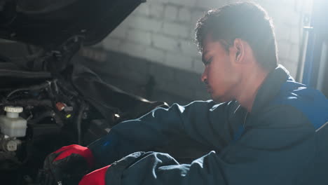 mecánico en uniforme azul trabajando en el motor del coche con toda la atención, la luz que brilla alrededor de su cabeza desde el fondo, la atmósfera enfocada destaca la habilidad y la experiencia en la reparación de automóviles