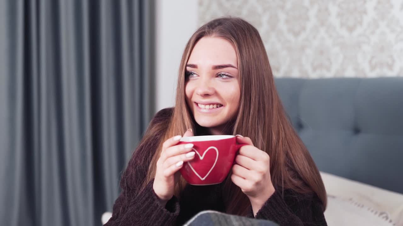 침실에서 침대에 앉아 차를 마시는 행복한 소녀