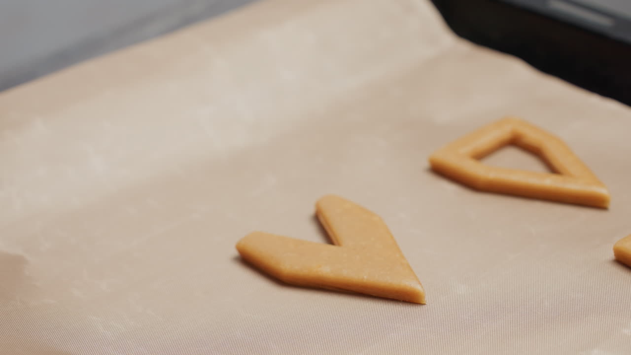 primer plano de una mujer usando un cortador de naranja para cortar la masa en formas en papel de pergamino en la cocina, preparando la masa para hornear con rodillo y otras herramientas de horneado visibles en el fondo