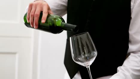 Mid-section-of-waiter-pouring-red-wine-into-a-wine-glass-at-counter