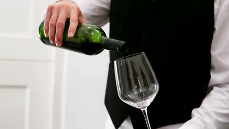 mid section of waiter pouring red wine into a wine glass at counter