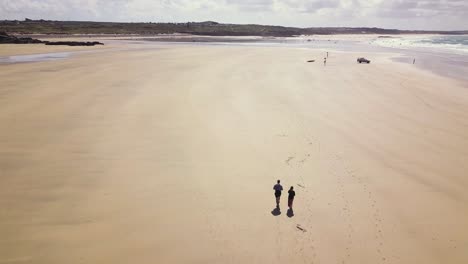 Aerial-View-Of-Beautiful-Seascape-With-Tourists-Walking-Along-The-Coast-Of-Sand-Beach-Of-Godrevy-In-Cornwall,-England---drone-shot