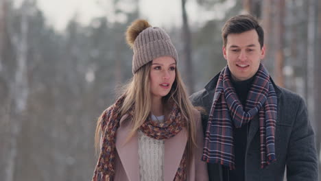 happy couple is playing winter game outside enjoying sunlight and warm winter weather in the mountains. strong boy is carrying girlfriend on his shoulders and whirls her