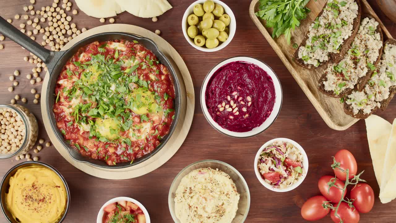 cocina israelí. shakshuka en sartén decorado con perejil, forshmak y hummus en la mesa, tomando aceitunas. platos nacionales judíos vista superior. huevos fritos en salsa de tomate, salsa, pita, cultura de oriente medio