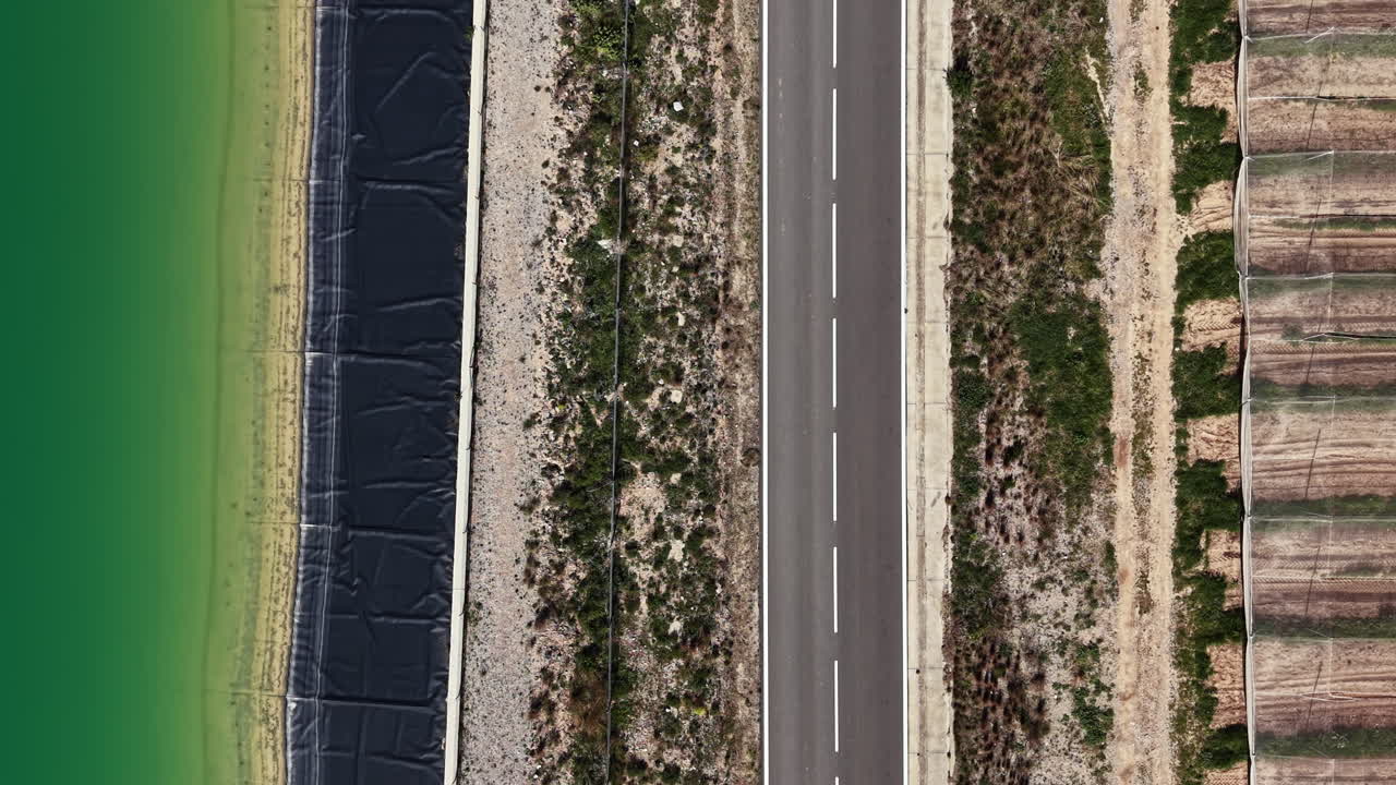 Autostrada che costeggia acqua verde con riva sabbiosa e terreni agricoli sullo sfondo durante il giorno soleggiato