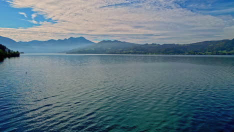 aerial drone forward moving shot over a large lake surrounded by mountain range on a cloudy day