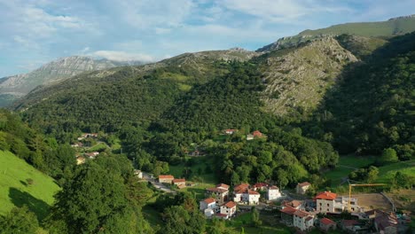 flight in a small and narrow valley in a village with meadows for crops and livestock with green grass with a background of a limestone mountain with a blue sky with clouds in cantabria-spain