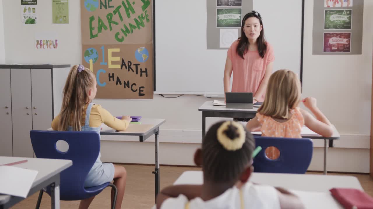 feliz maestra diversa con tableta enseñando a las escolares en el aula de la escuela primaria
