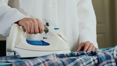 woman's hands ironing a plaid shirt