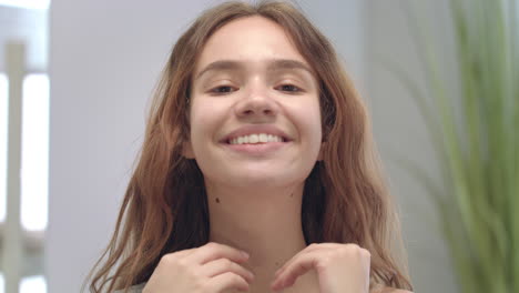 Happy-woman-doing-facial-massage-by-hands-and-looking-in-bathroom-mirror