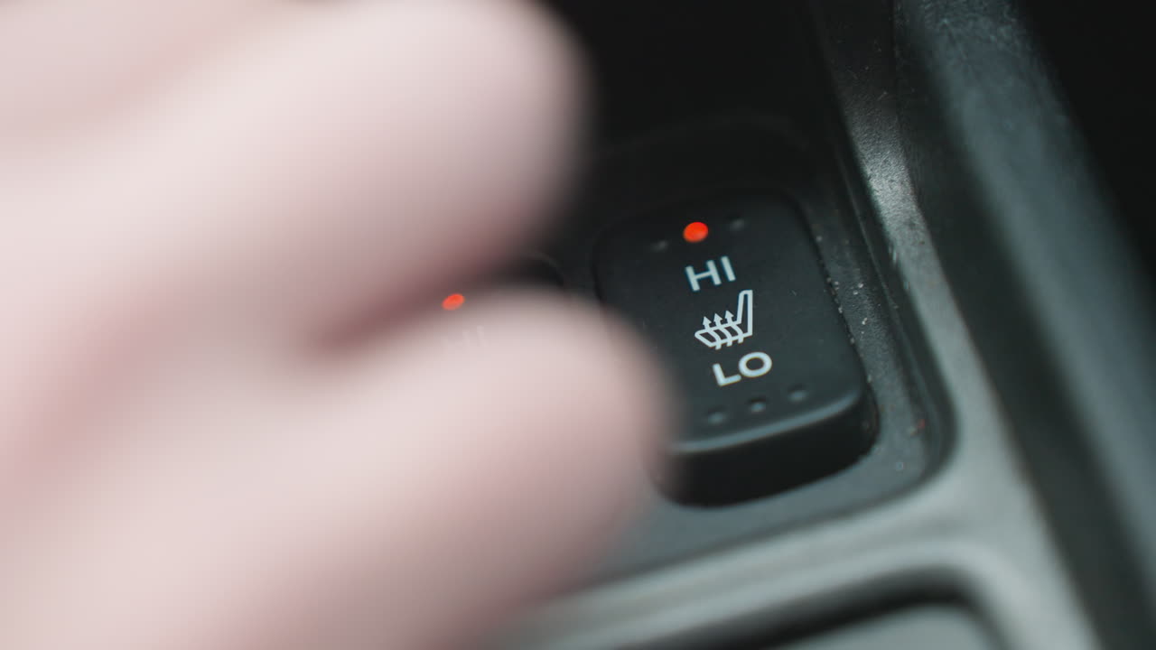 Close up of person pressing seat ac button with red indicator light on car console showing finger interaction with heating icon and modern interior control