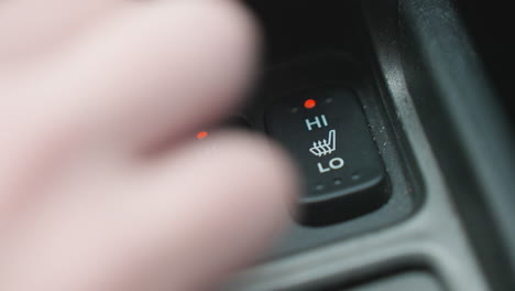 close up of person pressing seat ac button with red indicator light on car console showing finger interaction with heating icon and modern interior control