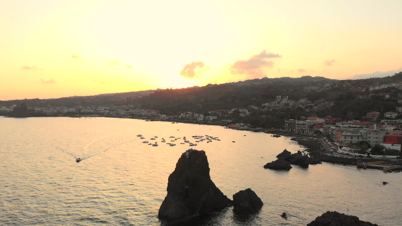 Aerial pullback, sunset over mountains behind coastal Italian town Acitrezza