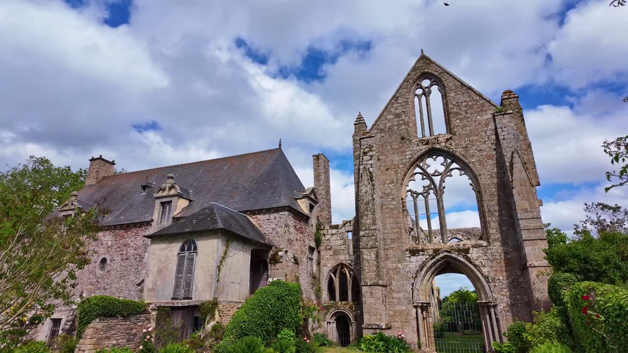 Ground pan shot of Beauport Abbey ruins in Paimpol under cloudy sky with a bird landing on the top