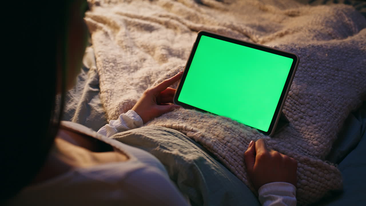 Wanita menggulir tablet layar hijau di kamar tidur pada malam hari, dari dekat. Wanita bekerja di malam hari.