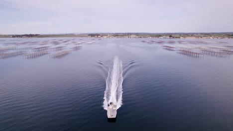 Aerial-drone-shot-of-a-motorboat-sailing-in-a-shellfish-farm-during-sunset-in-Sete,-France