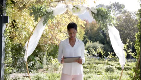 portrait of happy african american female wedding officiant holding tablet in garden, slow motion