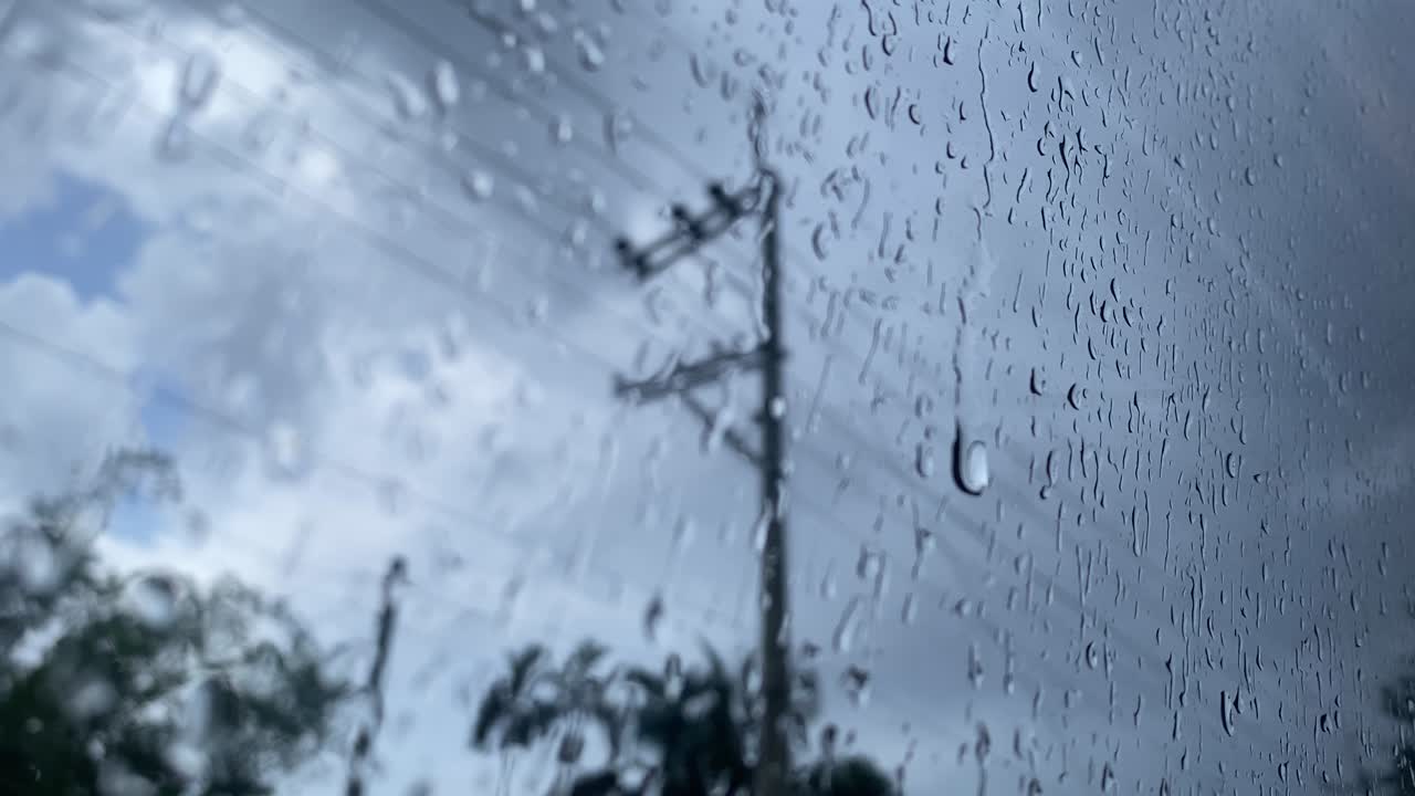Perspectiva de gotas de chuva no vidro da janela após chuva forte, com o céu nublado e desfocado lá fora