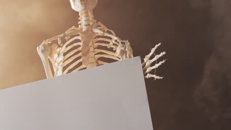 video of close up of halloween skeleton holding white board with copy space on brown background