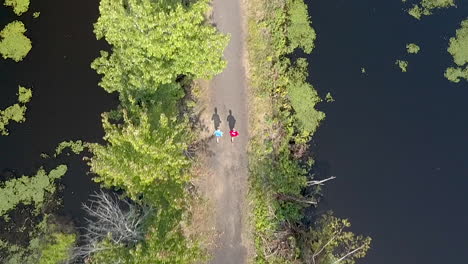 top down drone clip of two runners on a narrow path in the middle of a pond