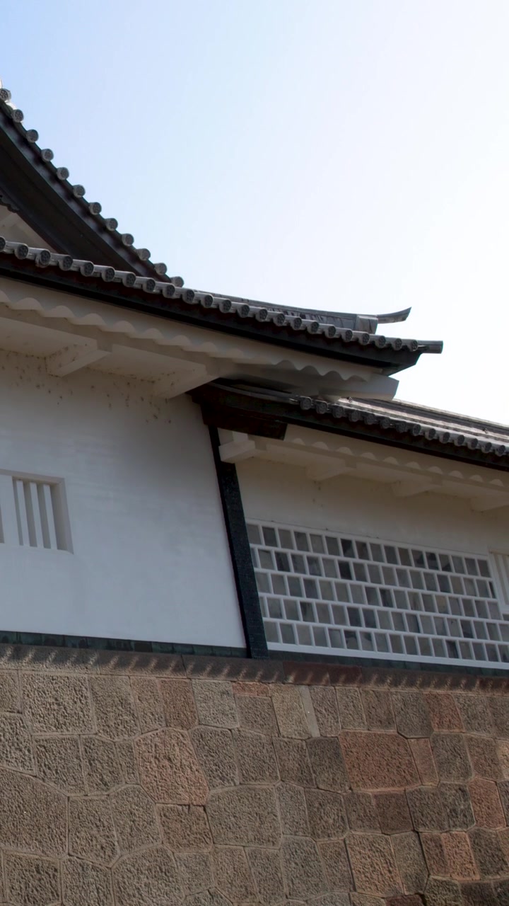 Statisk lavvinkeloptagelse af traditionel japansk slotsarkitektur mod en klar blå himmel.