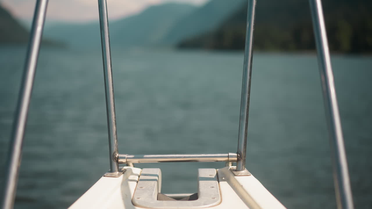 Stern with metal handrails on deck of sailing motor boat in sea against blurry mountains closeup. Back part of modern yacht with railings in ocean bay