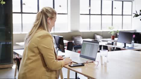 happy plus size caucasian casual businesswoman using laptop and earphones at desk