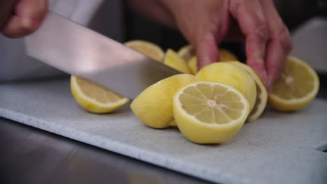 las manos femeninas usan un cuchillo grande para la mitad de cuatro limones en una tabla de cortar