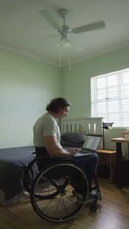 video vertical de un hombre discapacitado caucásico sentado en silla de ruedas usando una computadora portátil