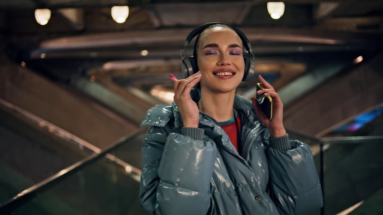 Ragazza con le cuffie che ascolta musica, tenendo lo smartphone in primo piano di notte. Donna che balla.