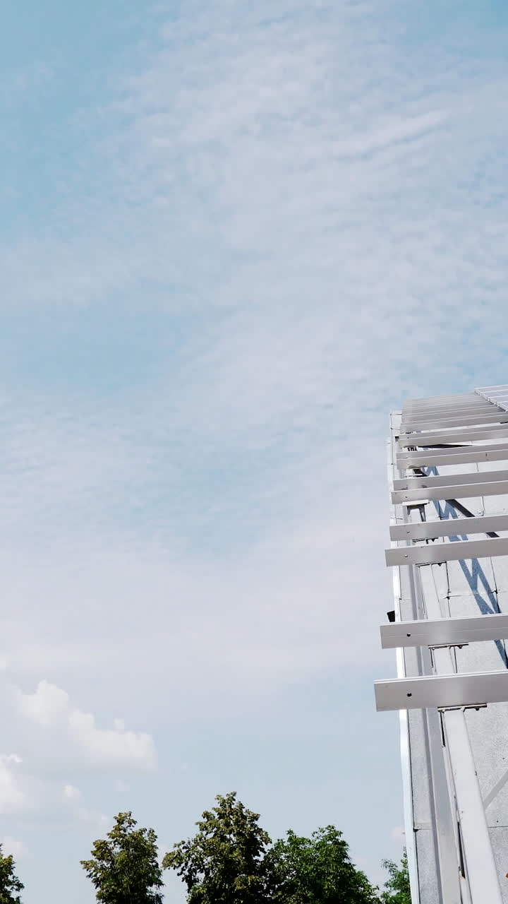 the structure of solar panels on the roof of the house against a blue sky with clouds. Vertical video
