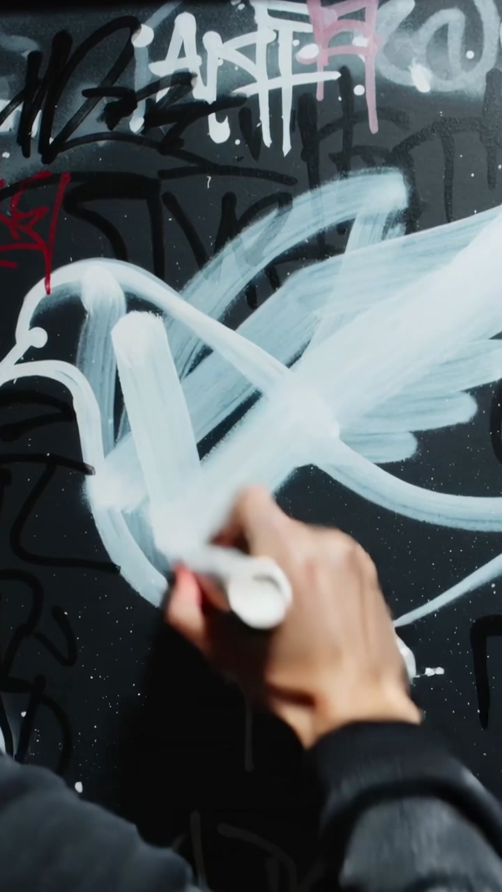 Vertical video: Bringing white pen, fur-hood artist painting bird as tag on black door, copy space