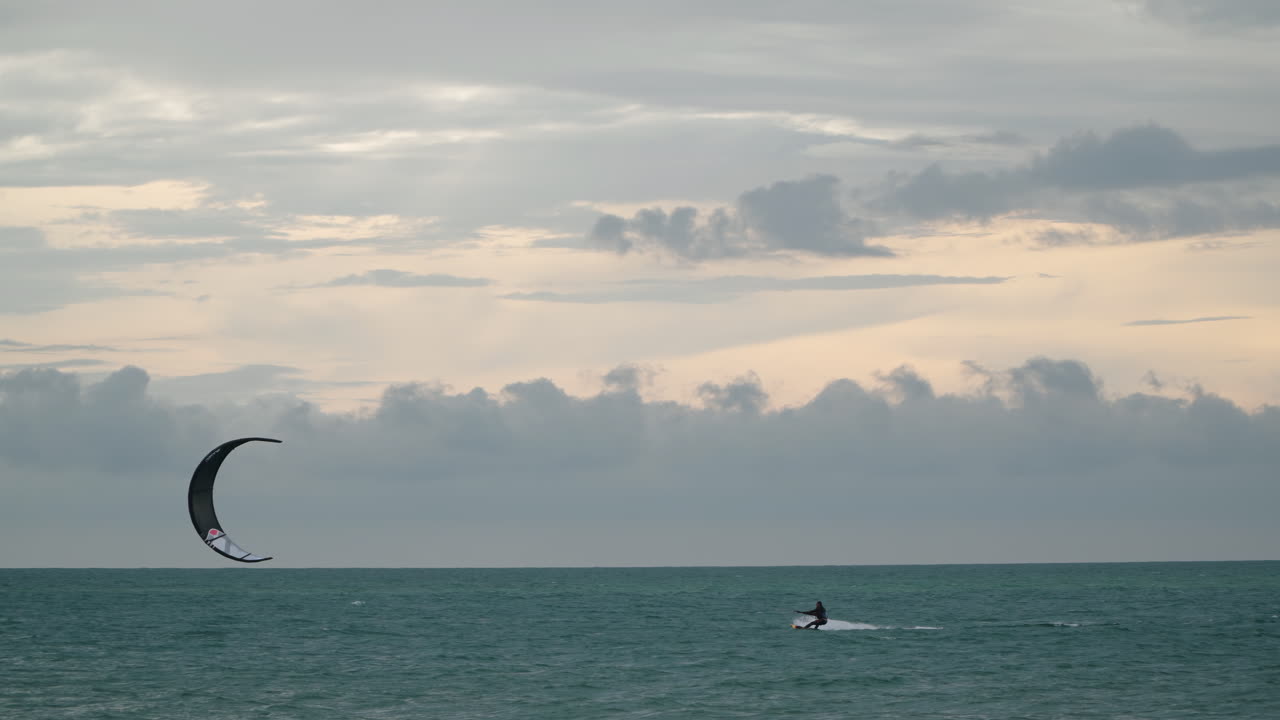 hombre haciendo kitesurf al atardecer contra un espectacular cielo nublado - tiro de seguimiento de gran angular