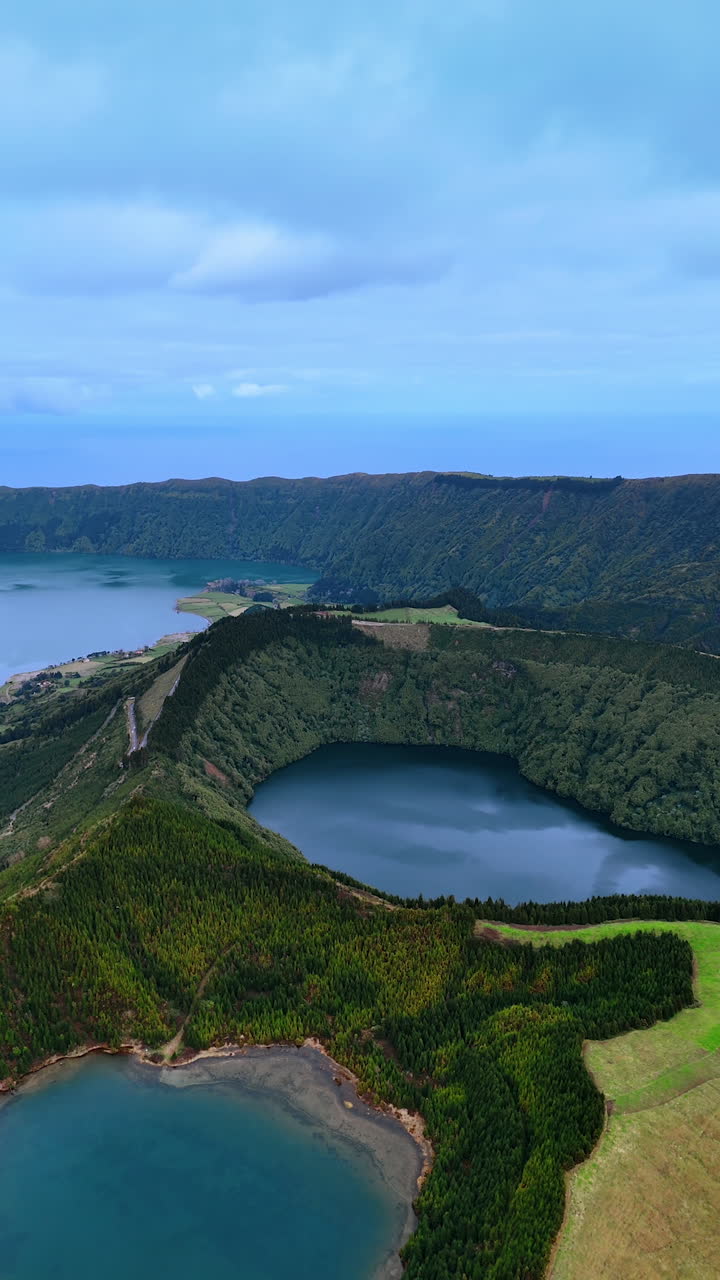 Flying above two craters of sleeping volcanoes with lakes inside. Scenic view of the Azorean Islands from top view. Vertical video.