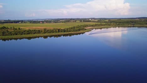 Aerial-shot-of-a-secluded-lake,-surrounded-by-fields-and-farms