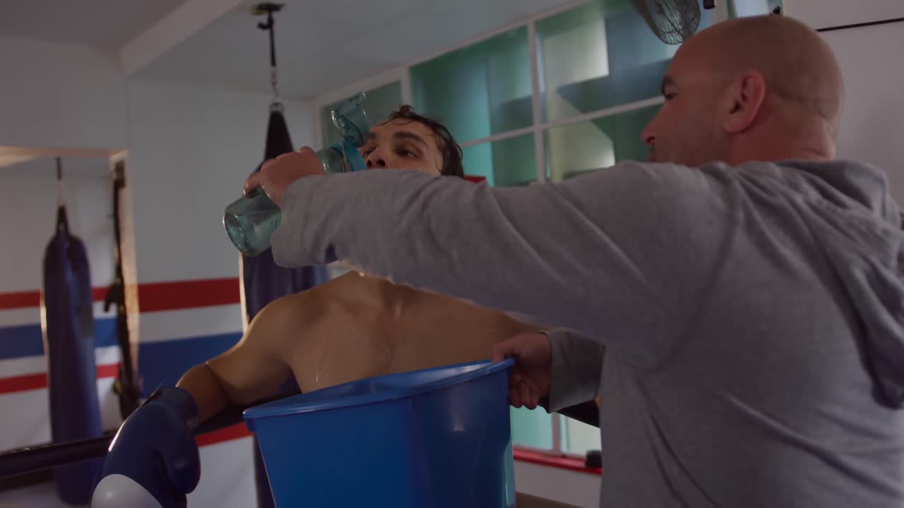 entrenador caucásico dando agua al atleta caucásico en el ring de boxeo