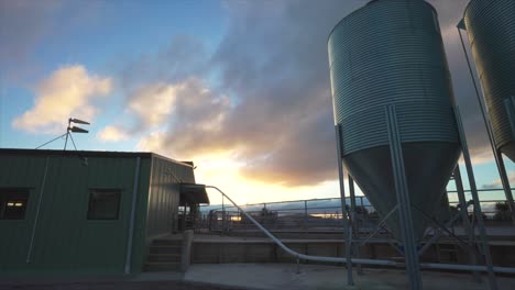 Puesta-De-Sol-En-La-Granja-De-Cobertizo-De-Ordeño-Con-Grandes-Silos-De-Acero-Inoxidable,-Timelapse